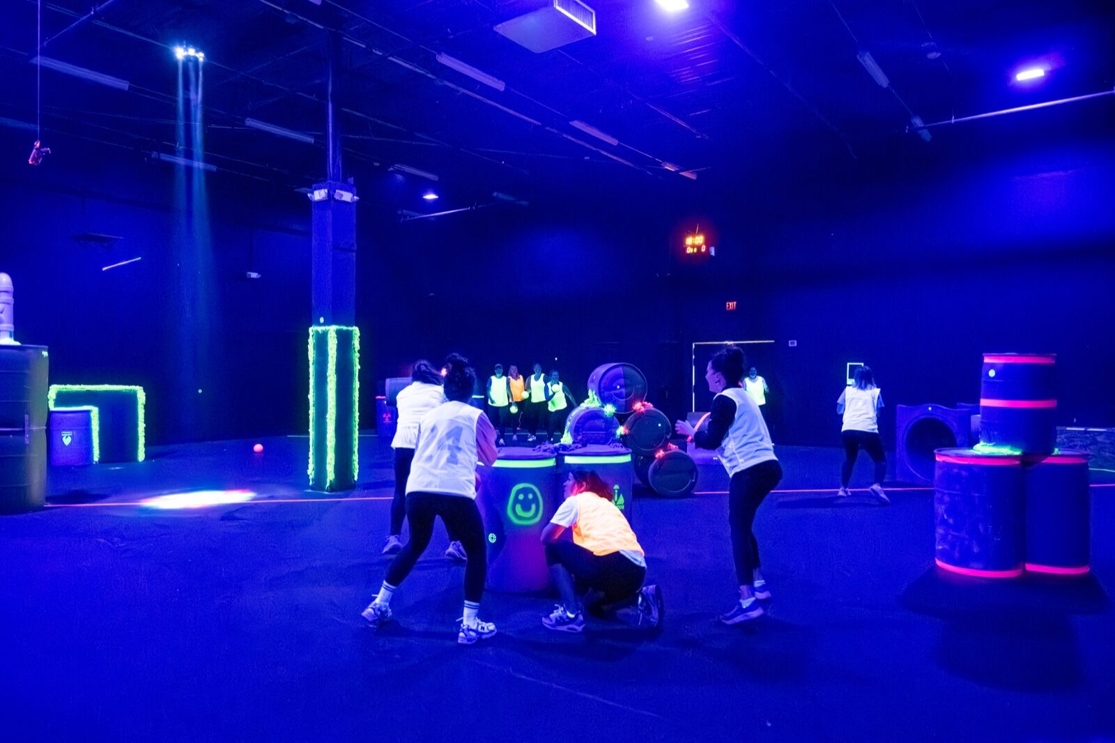 Players mid-game across the blacklit arena floor with glowing obstacles