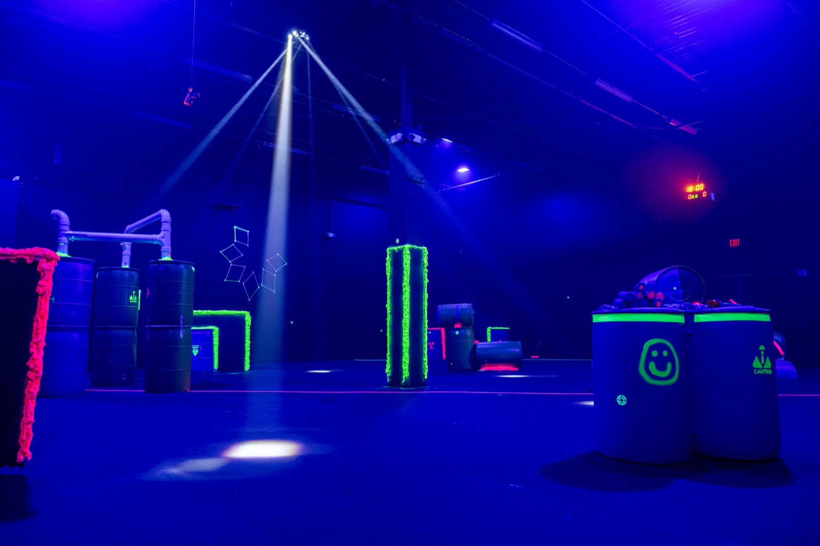 The empty blacklit arena with a spotlight beam, glowing pillar and smiley-face barrels