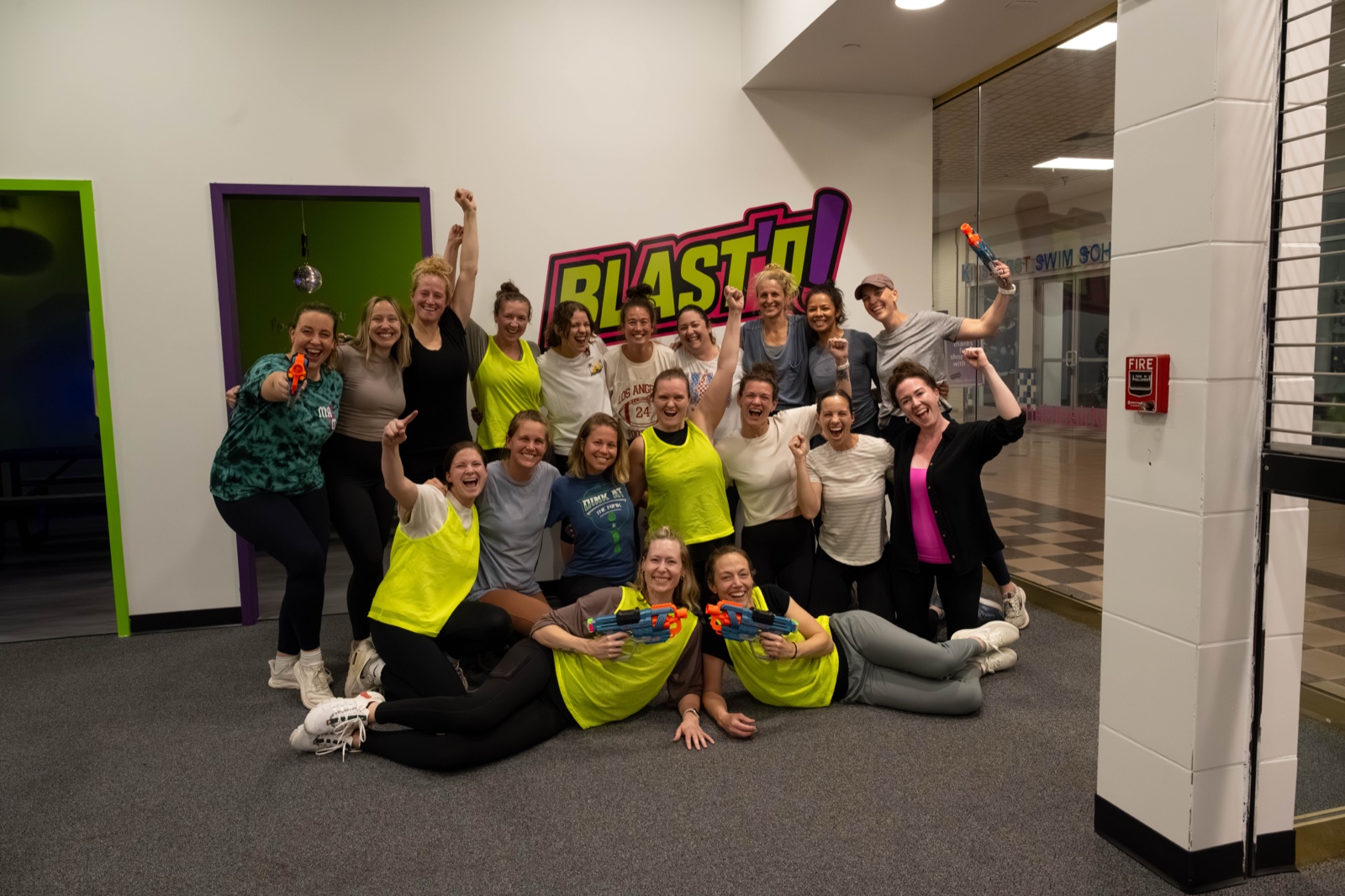 A large group of women holding foam blasters and cheering under the Blast'D! logo