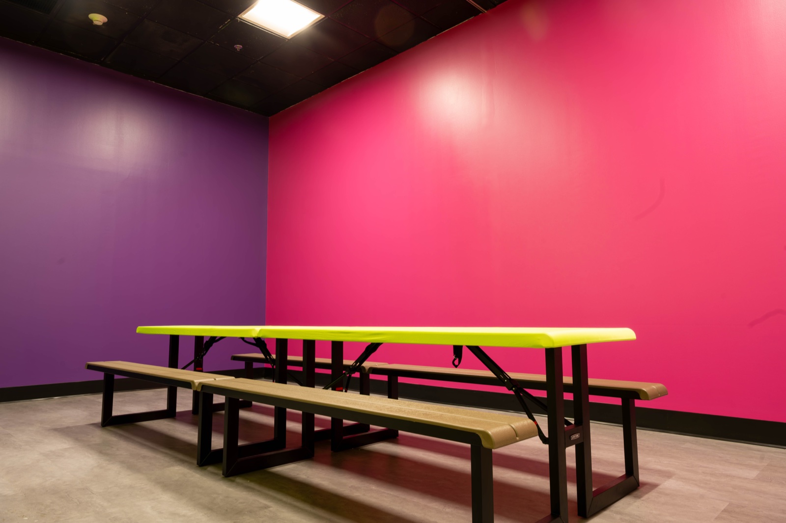 The Blast'D! private room with picnic tables against hot-pink and purple walls, set up flexibly for breakouts or catered lunch